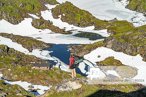 Junge Frau  Wanderin blickt auf See Isvatnet mit Eis  Berge und Schnee  Bergütte Trollfjord Hytta  am Trollfjord  Lofoten  Nordland  Norwegen  Europa