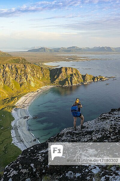 Hiker standing on rocks overlooking beach and sea  top of Måtinden mountain  near Stave  Nordland  Norway  Europe