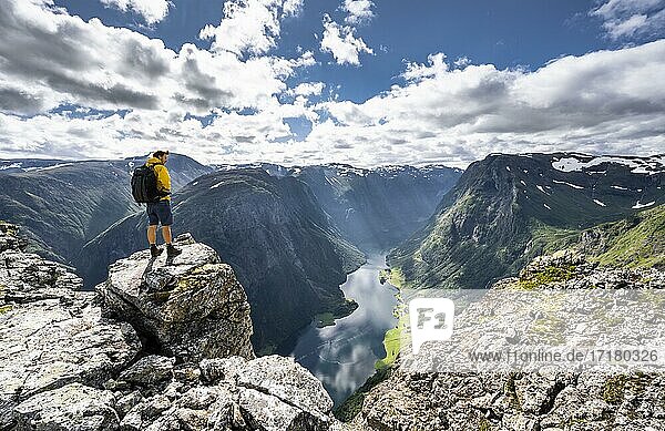 Wanderer steht auf Felsen  Blick vom Gipfel des Breiskrednosi  Berge und Fjord  Nærøyfjord  Aurland  Norwegen  Europa