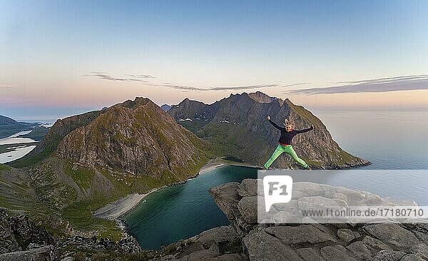 Junge Frau macht einen Luftsprung  auf dem Gipfel des Ryten  Meer  Kvalvika Strand und Berge  Fredvang  Lofoten  Nordland  Norwegen  Europa
