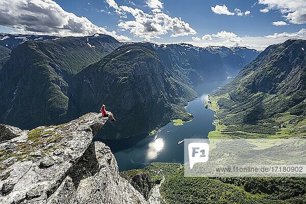 Wanderin sitzt auf Felszunge  Blick vom Gipfel des Breiskrednosi  Berge und Fjord  Nærøyfjord  Aurland  Norwegen  Europa