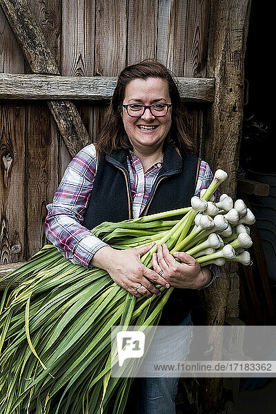 Lächelnde Frau hält einen Strauß frisch gepflückten Knoblauch.