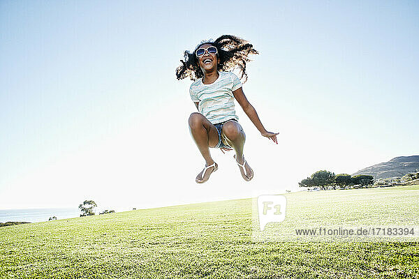 Junge gemischte Rasse Mädchen mit langen lockigen Haaren springt in der Luft
