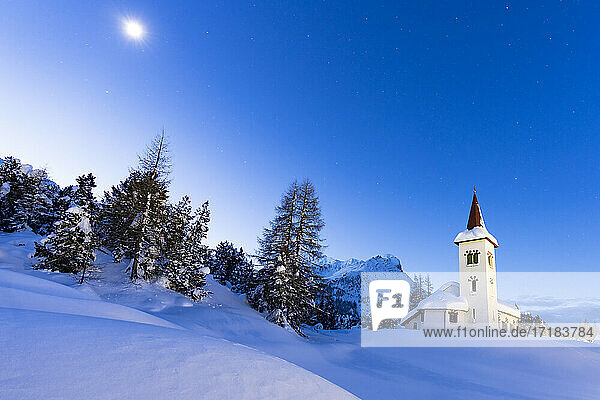 Abenddämmerung über Chiesa Bianca in der vom Mond beleuchteten Schneelandschaft  Maloja  Bergell  Engadin  Kanton Graubünden  Schweiz  Europa