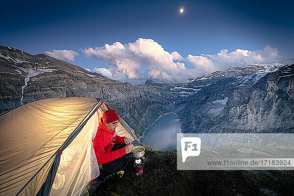 Hiker man with tent using camping stove on ridge above lake Limmernsee  Canton of Glarus  Switzerland  Europe