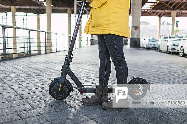 Young woman in yellow coat prepares and uses her electric skateboard.