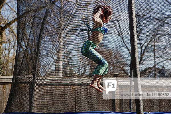 Ein kleines Mädchen in einem Meerjungfrauenkostüm springt barfuß auf einem Trampolin