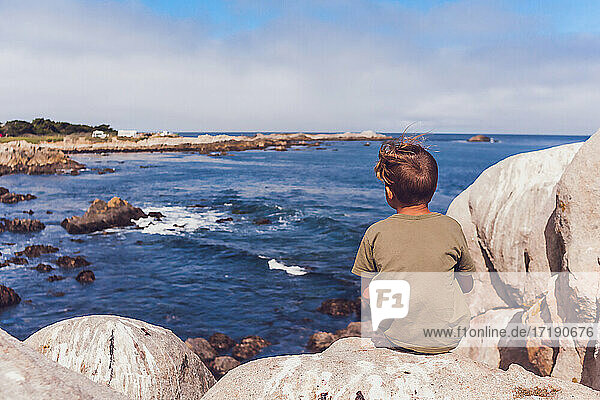 Kleiner Junge bewundert das Meer von einem großen Felsen aus.