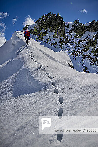 Ein Mann besteigt an einem sonnigen Tag einen verschneiten Berg in Devero  Italien.