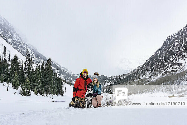 Glückliches Paar mit Vorstehhund auf schneebedecktem Feld gegen den Himmel im Urlaub