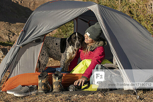 Lächelnde junge Frau mit Hund im Zelt auf einem Berg im Urlaub