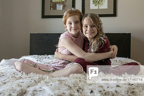 Two happy young girls having a feather pillow fight on the bed.