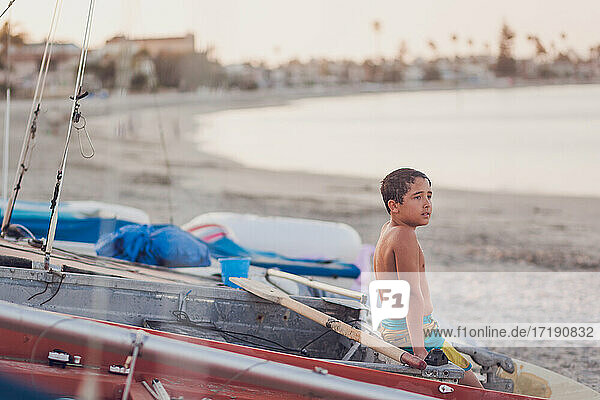 Young boy sitting on a docked boat at the beach.