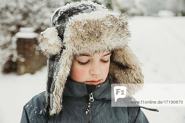 Portrait of boy looking down wearing furry hat in snow