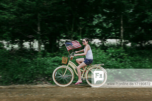 Girl Riding her Bike with an American Flag on a Rural Dirt Road