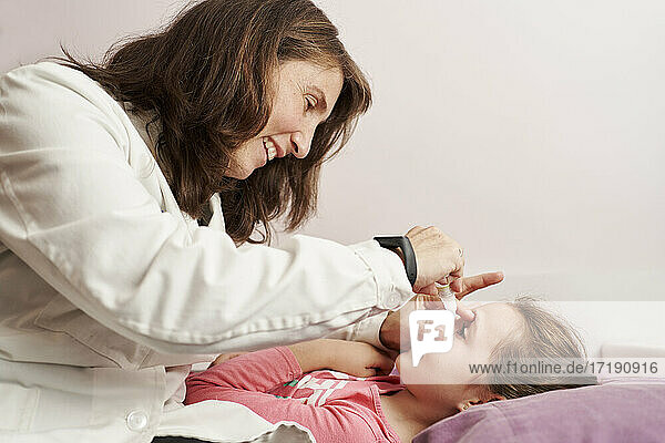 Eine Ärztin lächelt und gibt einem kleinen Mädchen in ihrem Bett Augentropfen. Hausarzt Konzept