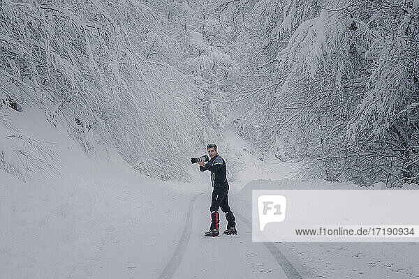 Fotograf bei der Arbeit auf einer verschneiten Straße im Wald
