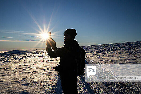 man trekking at taking pictures in winter sunset