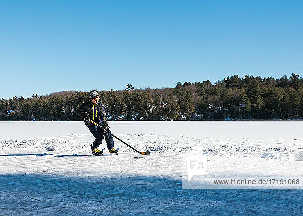 Teen boy playing hockey on an outdoor rink on a frozen lake in Canada.