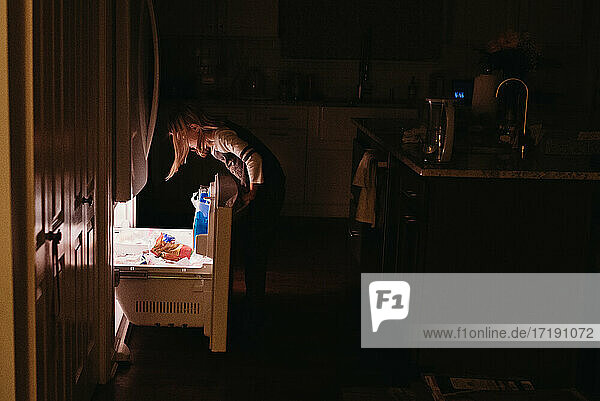 Tweener-Mädchen schaut in die Gefrierschublade in der dunklen Küche