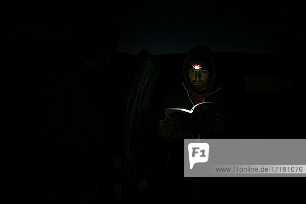 Mann  der bei Nacht im Canyonlands-Nationalpark im Schein einer Stirnlampe ein Buch liest