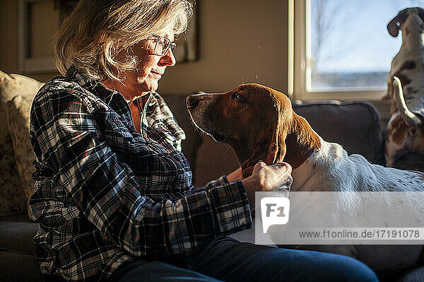 Glückliche Seniorin spielt mit Hundeohren auf der Couch zu Hause