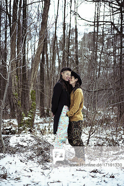 queer lesbian couple smile and cuddle in snow covered woods in germany