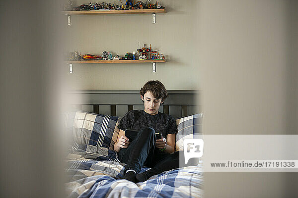 Blick durch die Tür auf einen kleinen Jungen  der mit einem Tablet auf seinem Bett sitzt.
