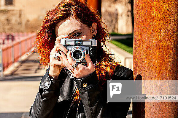 Alternatives Mädchen mit blauen Augen und orangefarbenen Haaren macht ein Foto mit ihrer Vintage-Kamera.