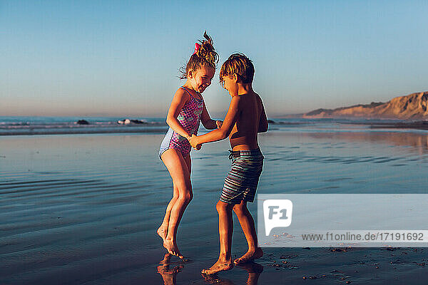 Boy and girl playing ring around the rose at the beach at golden hour.