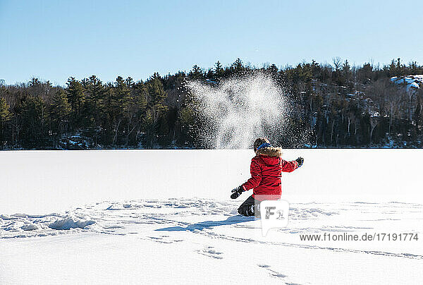Young boy throwing snow in the air in the middle of a frozen lake.