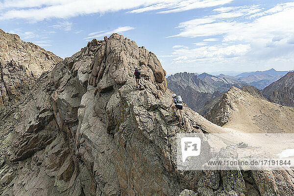 Freundinnen klettern auf Felsen beim Wandern auf einem Berg gegen den Himmel