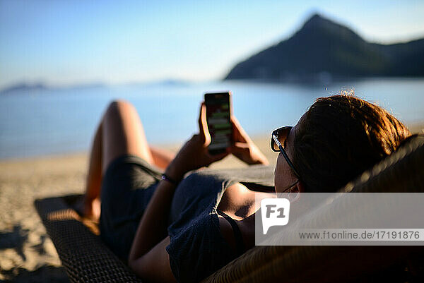 Junge Frau benutzt das Smartphone am Strand
