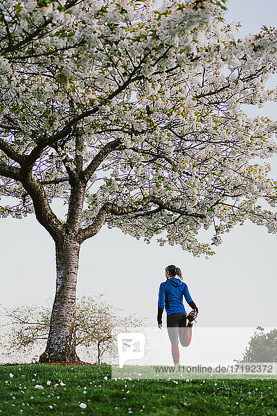 Eine sportliche Frau streckt ihre Beine unter einem Kirschblütenbaum in einem Park aus