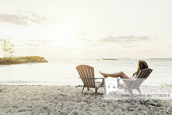 junge Frau am Strand sitzend bei Sonnenuntergang auf den Bahamas