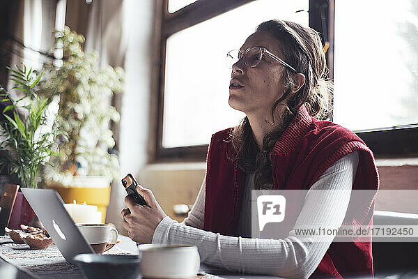 Frau spricht während eines Treffens zu Hause mit Telefon und Laptop in Pandemie