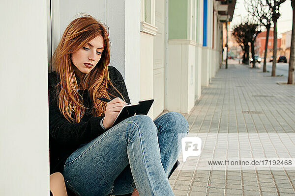 Junge Frau schreibt in ihr Notizbuch  während sie auf der Straße sitzt