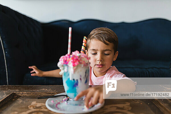 Ein kleiner Junge isst die Süßigkeiten aus einem bunten Milchshake.