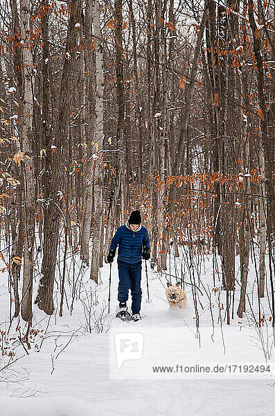 Teenager mit Hund auf Schneeschuhen im Wald an einem verschneiten Wintertag.