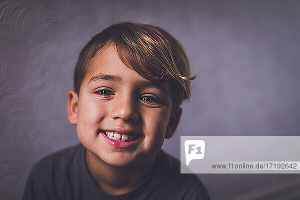 Ein lächelnder Junge mit haselnussbraunen Augen schaut in die Kamera.