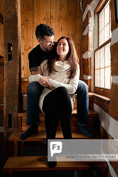 Glückliches Paar sitzt zusammen auf einer Treppe in einem rustikalen Blockhaus.
