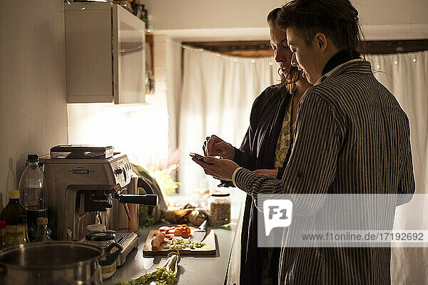 Homosexuelles Paar folgt Telefonrezept in der Küche und kocht gesundes Abendessen
