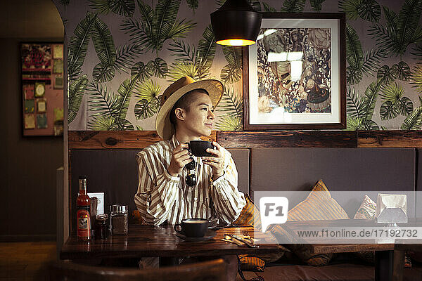 Alternativer androgyner junger Reisender mit Hut trinkt Kaffee in einem Cafe