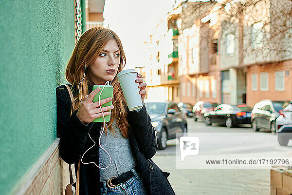 Geschäftsfrau hält eine Kaffeetasse  während sie auf ihr Telefon schaut