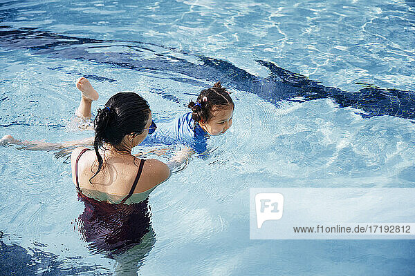 Mother assisting her daughter to swim in swimming pool