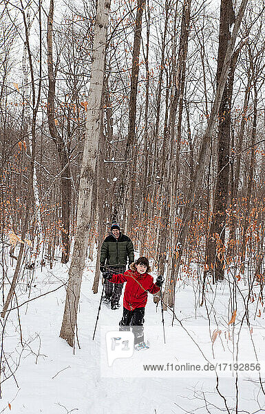 Young boy snowshoeing with father in the woods on a snowy winter day.