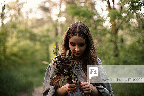 Teenage girl holding bouquet of wild flowers standing in forest