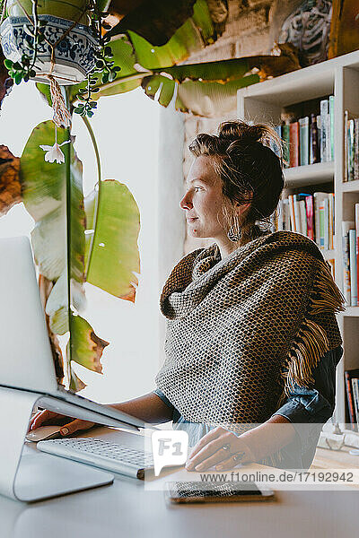 Stilvolle Frau arbeitet an ihrem Laptop im Büro zu Hause  umgeben von Pflanzen