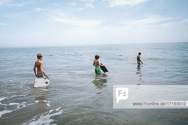 Drei Jungen stürzen sich mit Boogie Boards in den Ozean