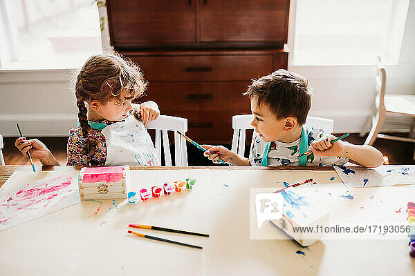 Bruder und Schwester sitzen am Tisch und malen mit Regenbogenfarben